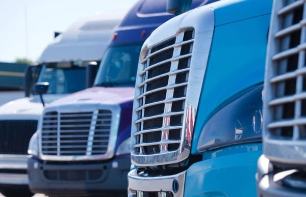 Grilles of different models of big rig semi trucks which stand in row on the truck stop parking waiting to continue delivery cargo