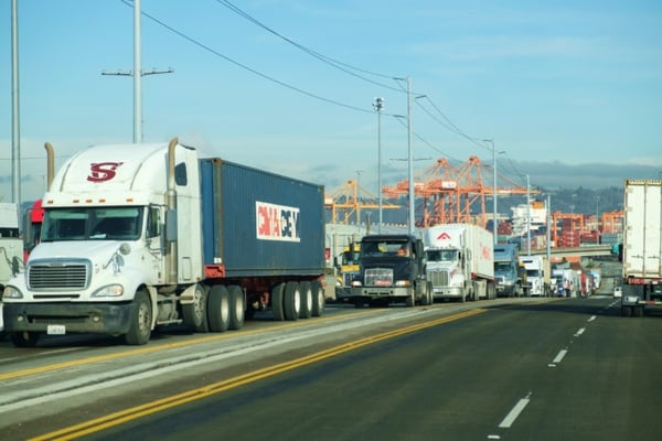 Tacoma, WA, USA Jan. 23, 2017: Long line of semi trucks leaving Port of Tacoma shipping terminals with orange cranes in background